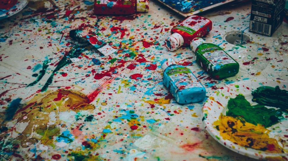 drops of different colored paint cover these paint bottles, canvas, plate, and more.